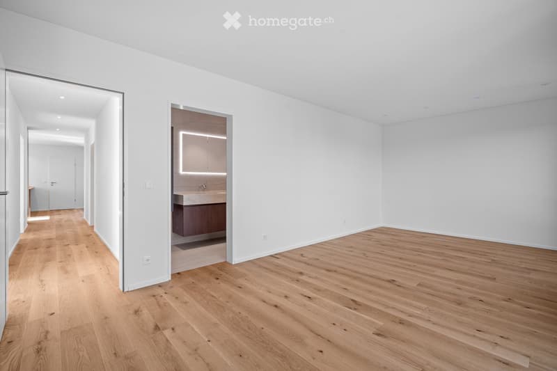 Empty room with light wooden flooring and white walls, featuring a partially visible adjacent bathroom with a sink and cabinet.