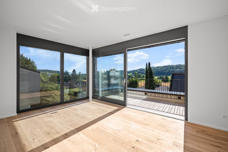 Bright, unfurnished room with large glass sliding doors leading to a balcony, wooden flooring, and white walls.