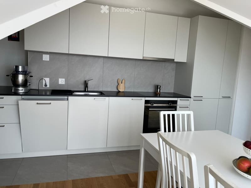 Modern kitchen with white cabinets, stainless steel appliances, a sink, a mixer, and a dining area with a white table and chairs.
