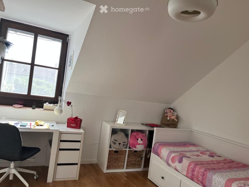Cozy bedroom with a lofted bed, desk, and storage unit. Features a large window with blinds, a modern lamp, and decorative items on shelves.