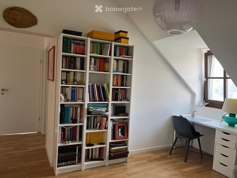 A cozy study or home office with a large bookshelf filled with books, a modern desk with a chair, and a window letting in natural light.