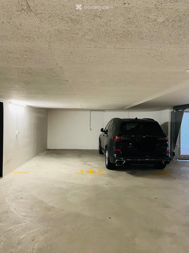 Underground parking space with a single parked car, marked parking lines, and concrete floors and walls.