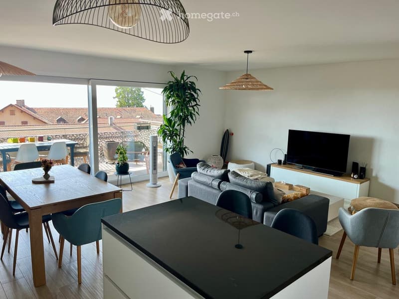 Modern living and dining area with a grey sofa, coffee table, dining table with chairs, TV, and a large plant near the balcony.