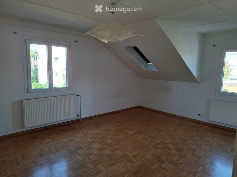 Empty room with wooden flooring, white walls, and large windows. Features a skylight and radiators on both sides.
