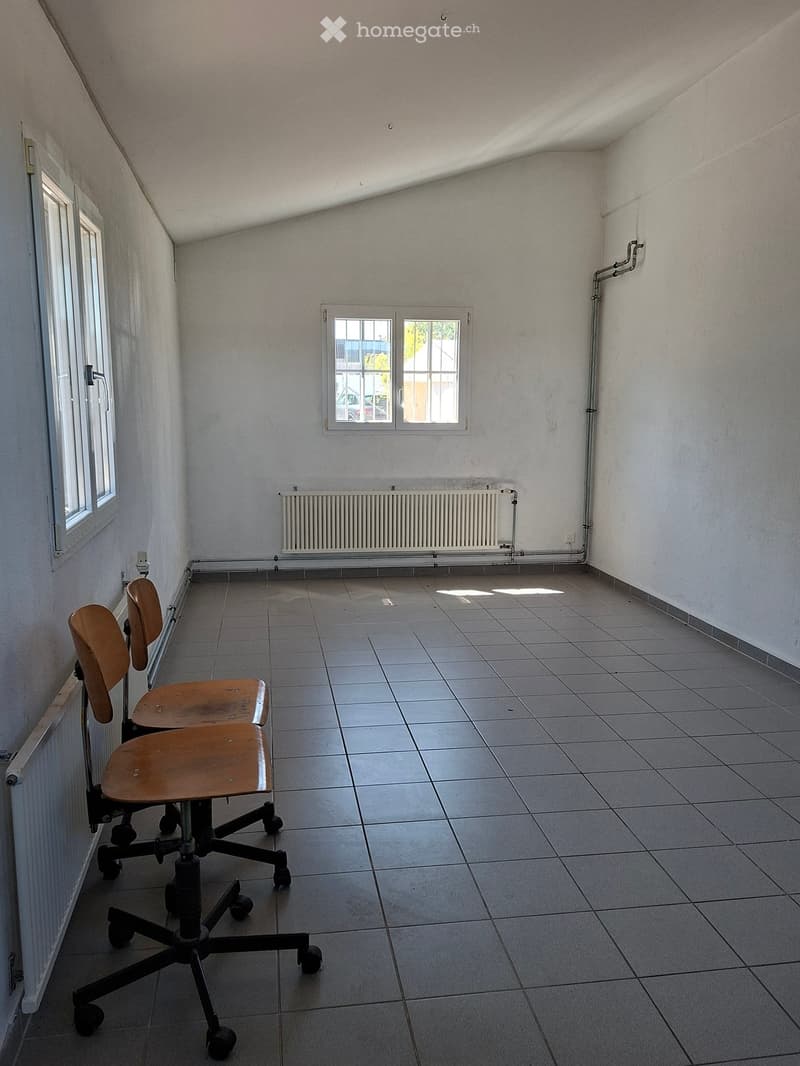 An unfurnished room with tiled flooring, white walls, and a radiator. Two chairs are positioned near the window.