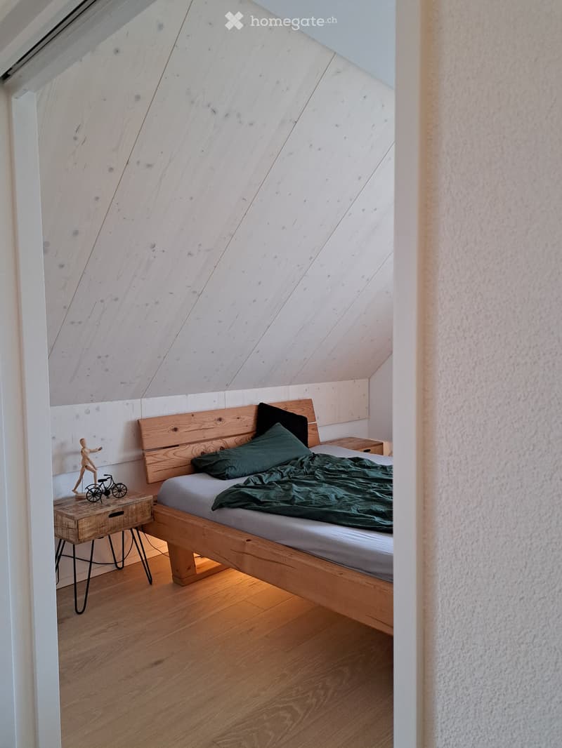 Cozy attic bedroom with wooden bed, nightstand, and small wooden stool holding a toy and bicycle model.