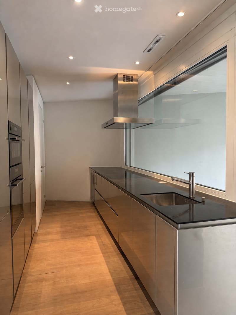 Modern kitchen with stainless steel appliances, black countertops, and wooden flooring.