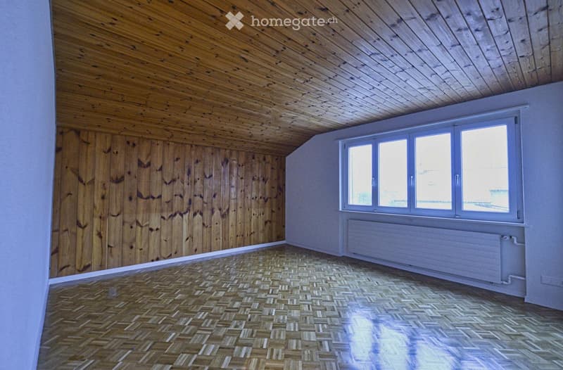 Empty room with wooden walls, herringbone wooden floor, and large windows with white frames. No furniture or equipment present.