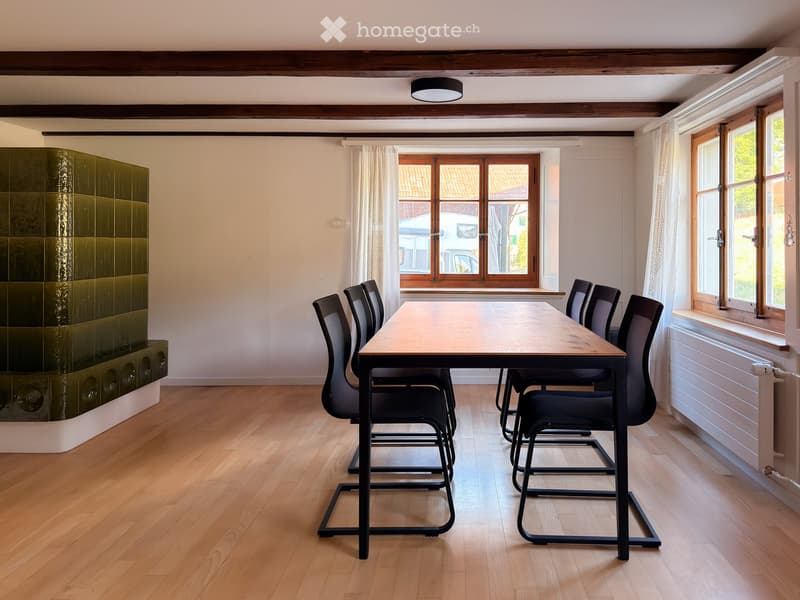 Dining room with wooden floor, modern dining table, six chairs, large windows, radiator, and a green tiled wall.