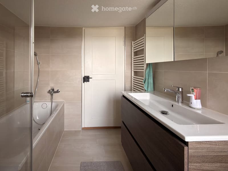 Modern bathroom with a bathtub, double sink, mirror, radiator, and a towel hanging on the radiator.