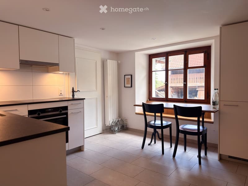 Modern kitchen with white cabinets, stainless steel appliances, and a dining area with two chairs and a table.