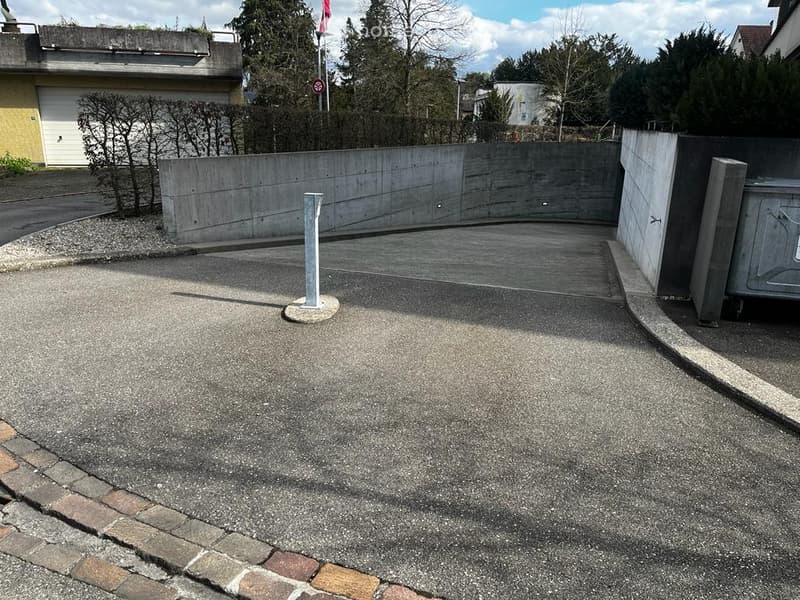 Empty parking area with concrete walls and a single pole, adjacent to a garage and residential building.