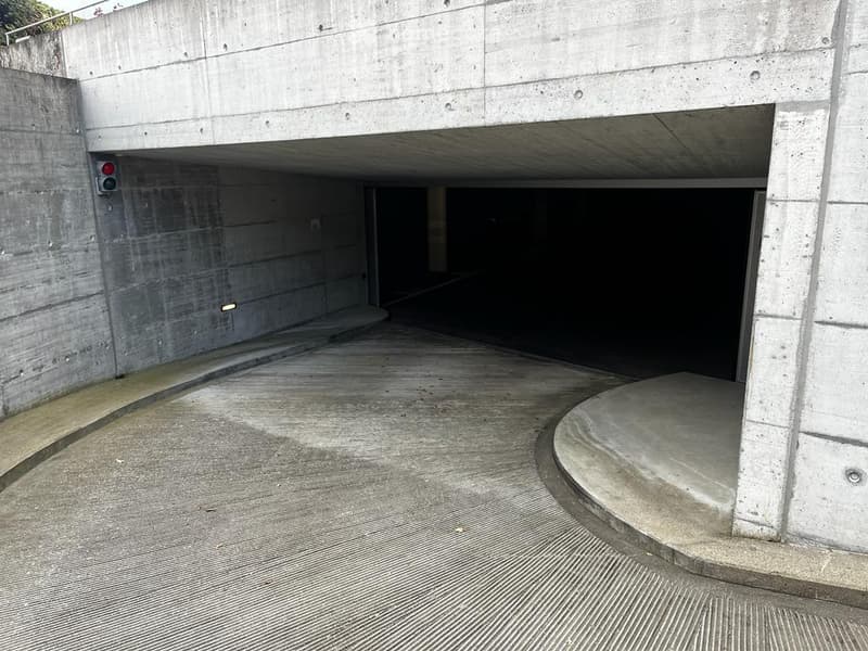 Underground garage entrance with concrete walls and a traffic light signal visible on the left side.