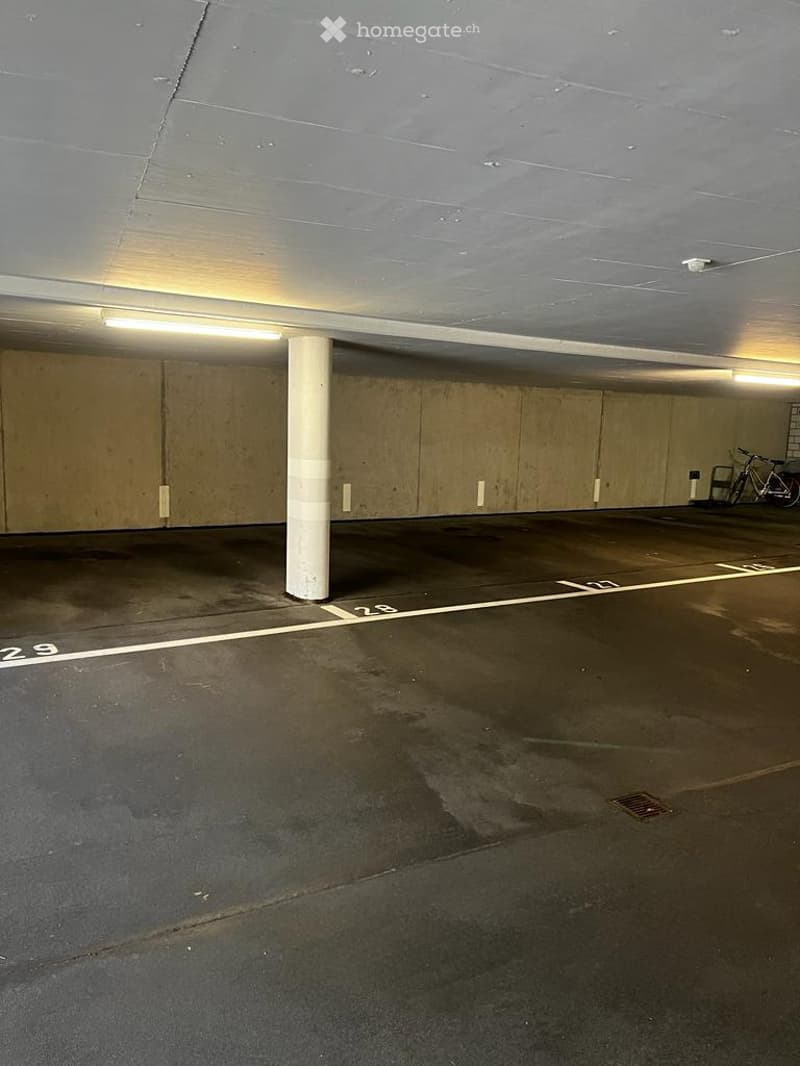 Underground parking area with marked parking spaces, a central support column, and a bicycle parked against the wall.