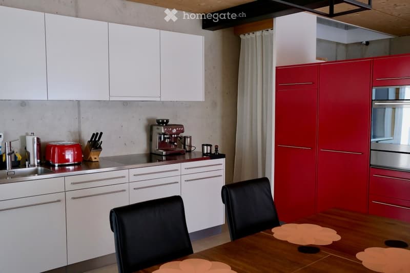Modern kitchen with white and red cabinets, stainless steel appliances, a wooden dining table with chairs, and various kitchen items on the counter.