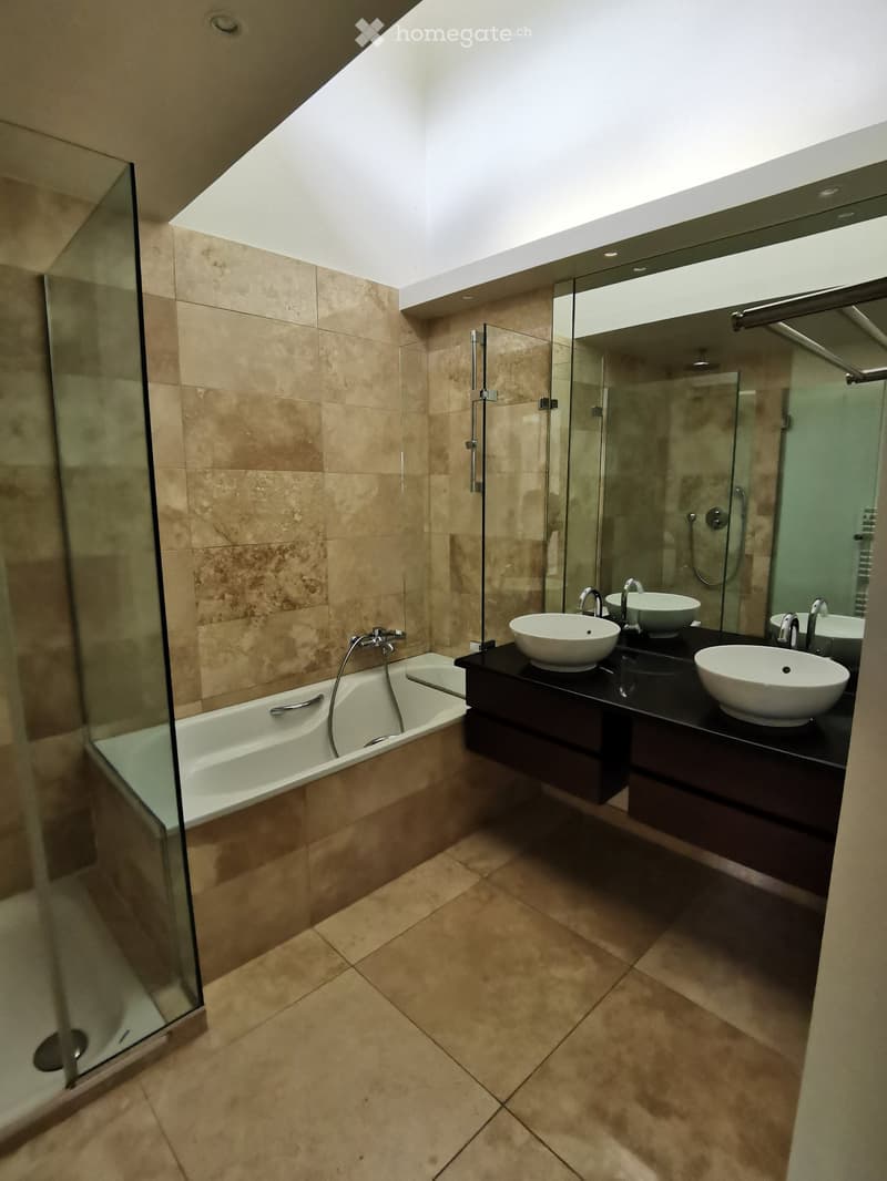 Modern bathroom with beige tiles, a bathtub, a double sink vanity with two round sinks, and a large mirror above the sinks.