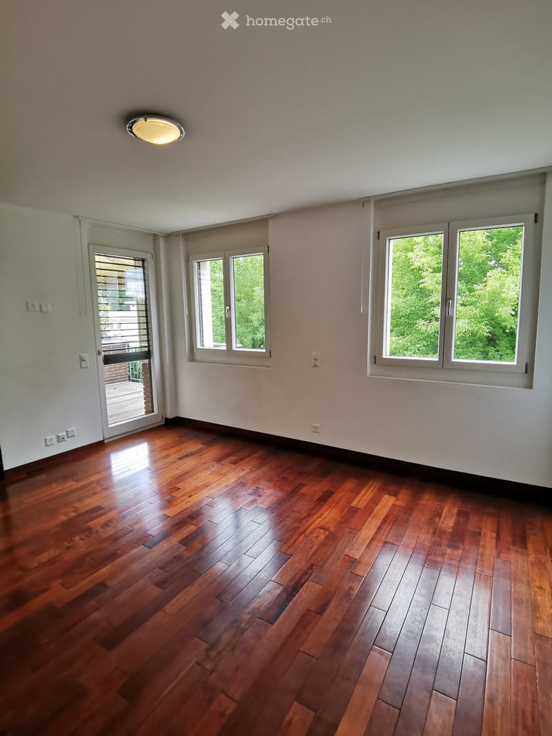 Empty room with wooden flooring, large windows, and a sliding glass door leading to a balcony.