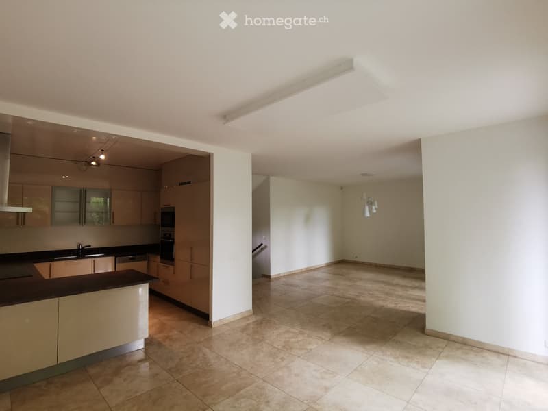 Open-plan kitchen and living area with modern cabinets, a sink, and an oven. The living area has a tiled floor and is connected to the kitchen by an open doorway.