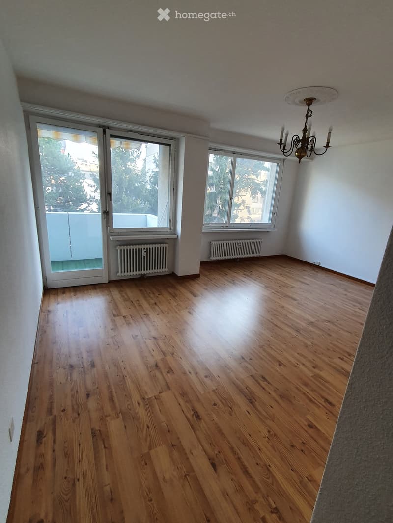 Empty room with wooden flooring, large windows, radiators, and a chandelier.