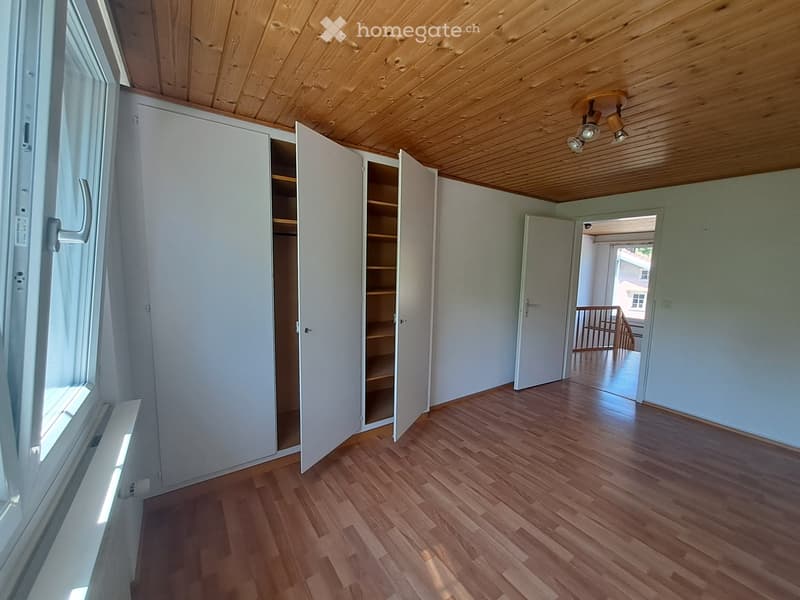 Empty room with wooden flooring, white walls, built-in closet with open shelves, and a doorway leading to a balcony area.