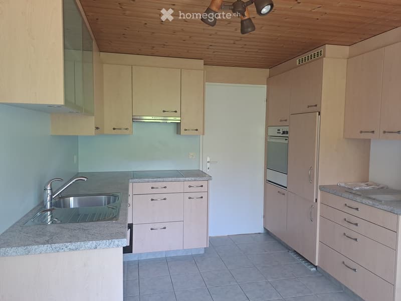 Modern kitchen with light wood cabinets, granite countertops, stainless steel sink, and built-in oven.
