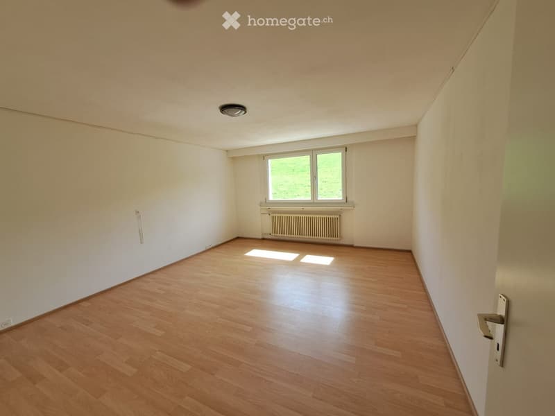 Empty room with wooden flooring, white walls, a window with white frame, and a radiator below the window.