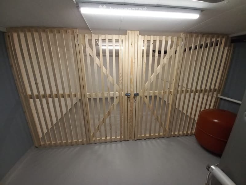 A narrow, unfinished corridor with a wooden slatted wall and a red cylindrical object on the right side.