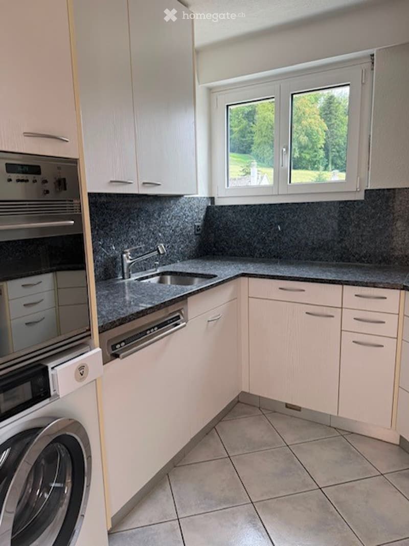 Modern kitchen with white cabinets, granite countertops, stainless steel sink and dishwasher, and a washing machine visible.