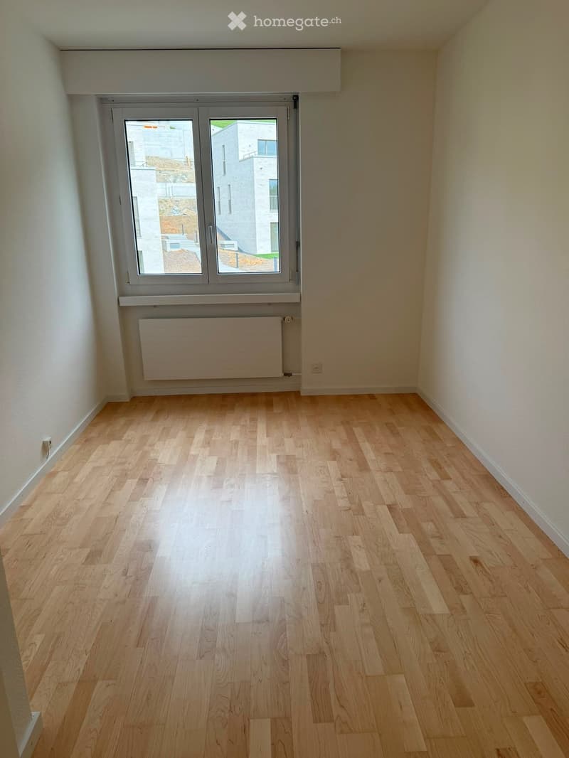 Empty room with light wooden flooring, white walls, and a large window with a radiator below it.