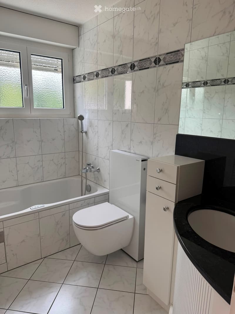 Modern bathroom with marble tiles, bathtub, toilet, sink, and cabinet.