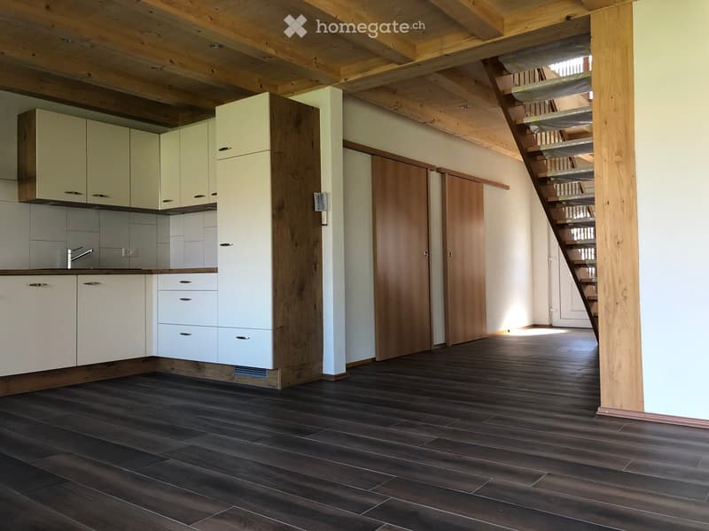 Modern kitchen with light-colored cabinets, dark wooden flooring, and a visible staircase leading to an upper level.