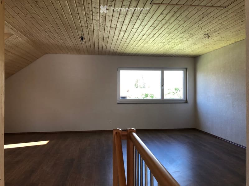 Empty room with wooden floor, slanted wooden ceiling, and a window letting in natural light. No furniture or equipment is present.