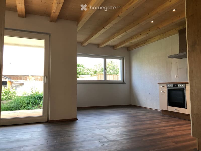 Modern kitchen with wooden flooring, exposed wooden beams on the ceiling, large windows, and built-in oven.