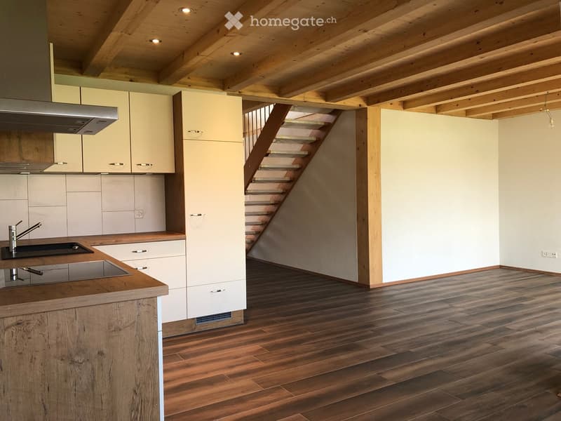 Modern kitchen with light-colored cabinets, wooden countertops, and a staircase leading to an upper level.