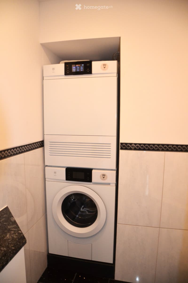 A compact bathroom with a white washing machine and a white dishwasher stacked vertically, featuring a digital control panel and a sleek design.