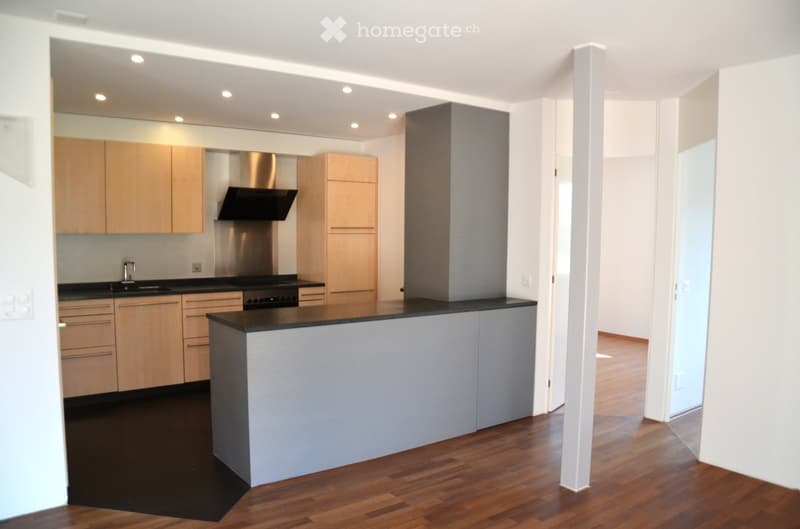 Modern kitchen with light wood cabinets, black countertops, stainless steel appliances, and a central island.