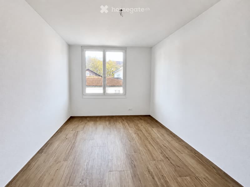Empty room with white walls, wooden flooring, and a large window offering a view of the outside.