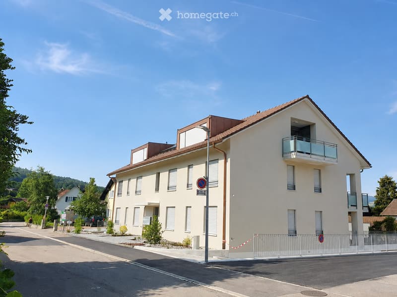 Two-story house with a modern design, light-colored facade, multiple windows, and a balcony on the upper floor.