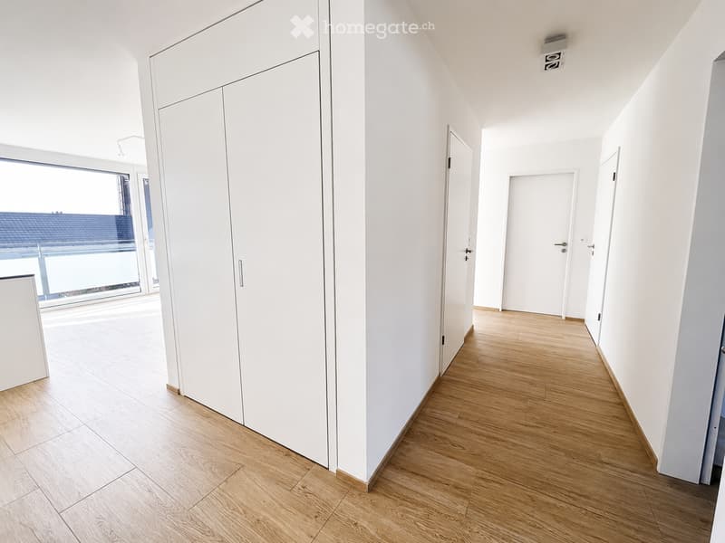 Bright, minimalist hallway with light wooden flooring, white walls, and several closed doors leading to other rooms.