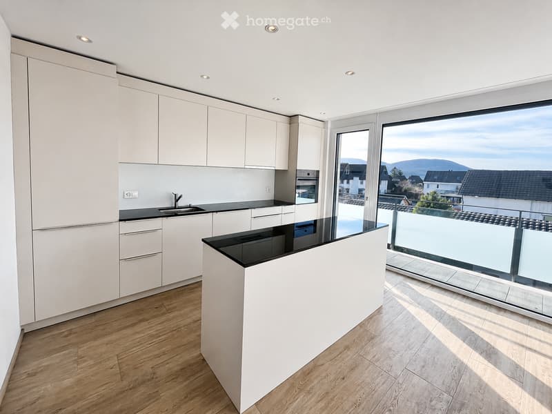 Modern kitchen with white cabinets, black countertops, and a central island, featuring large windows with a scenic mountain view.