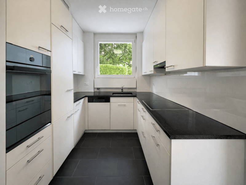Modern kitchen with white cabinets, black countertops, and black tiled floor. Features a sink, faucet, oven, and dishwasher.