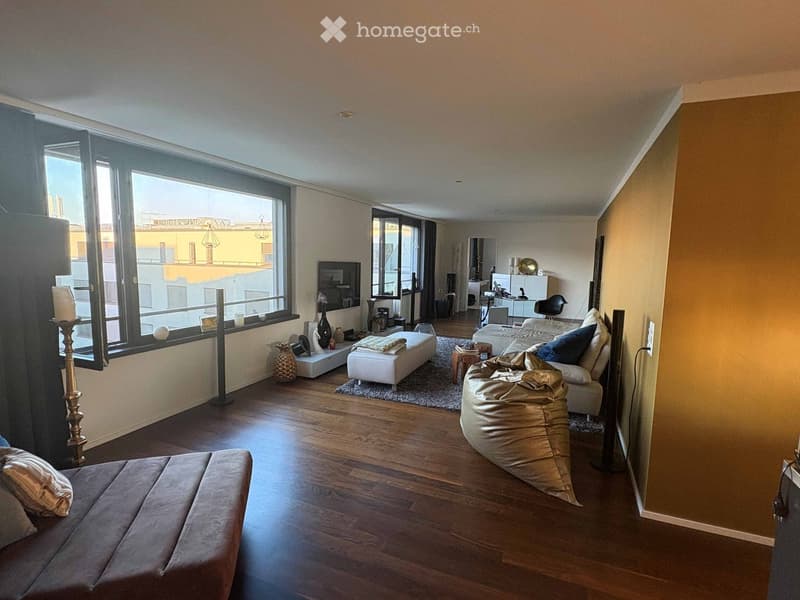 Modern living room with wooden flooring, large windows, a sofa, bean bag chair, ottoman, coffee table, and decorative items including candles and vases.