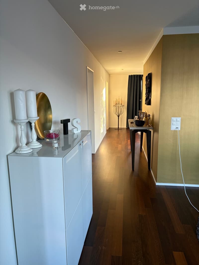 Modern hallway with wooden flooring, white walls, and decorative items including a console table, candles, and a small table with framed photos.