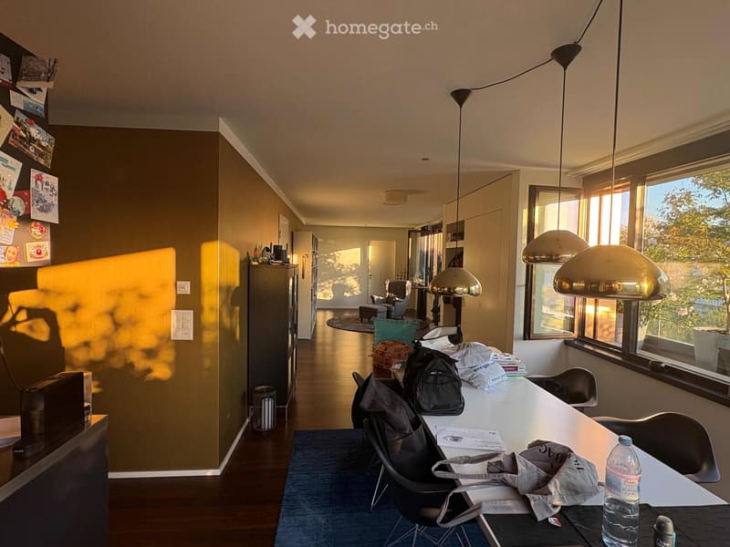 Bright, modern room with large windows, wooden floor, and contemporary furniture including a table, chairs, and a sofa area.
