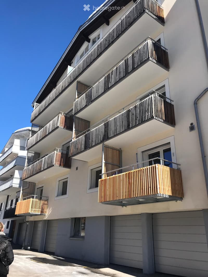 Modern multi-story residential building with balconies, wooden railings, and large windows.