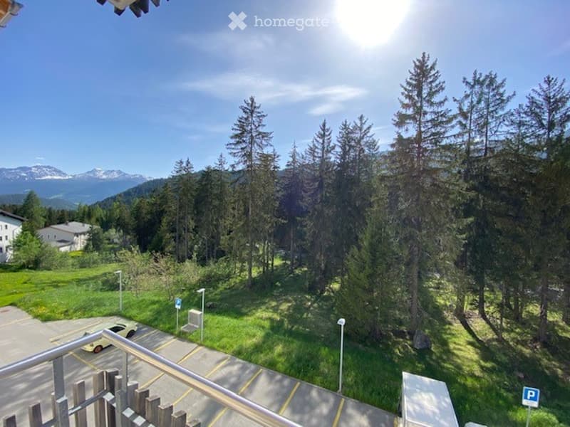 Balcony overlooking a green, tree-filled area with distant mountains under a clear blue sky.