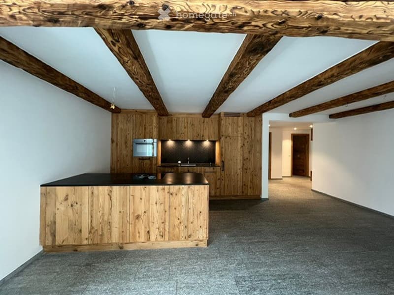 Modern kitchen with wooden cabinets, a central island, and built-in appliances, featuring exposed wooden beams on the ceiling.