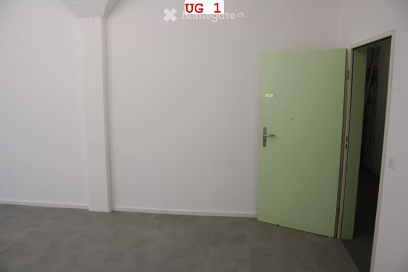 Empty room with white walls, grey tiled floor, and a green door leading to another space.