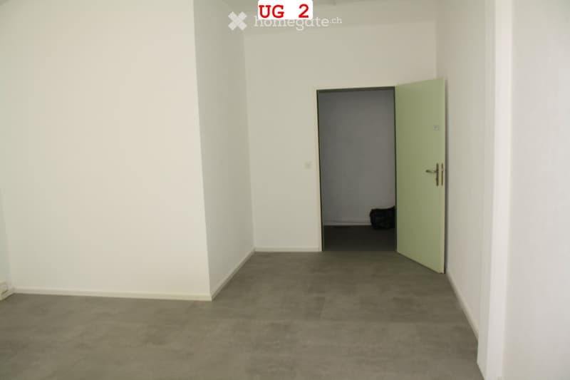 Empty room with white walls and a concrete floor, featuring an open doorway leading to another room.