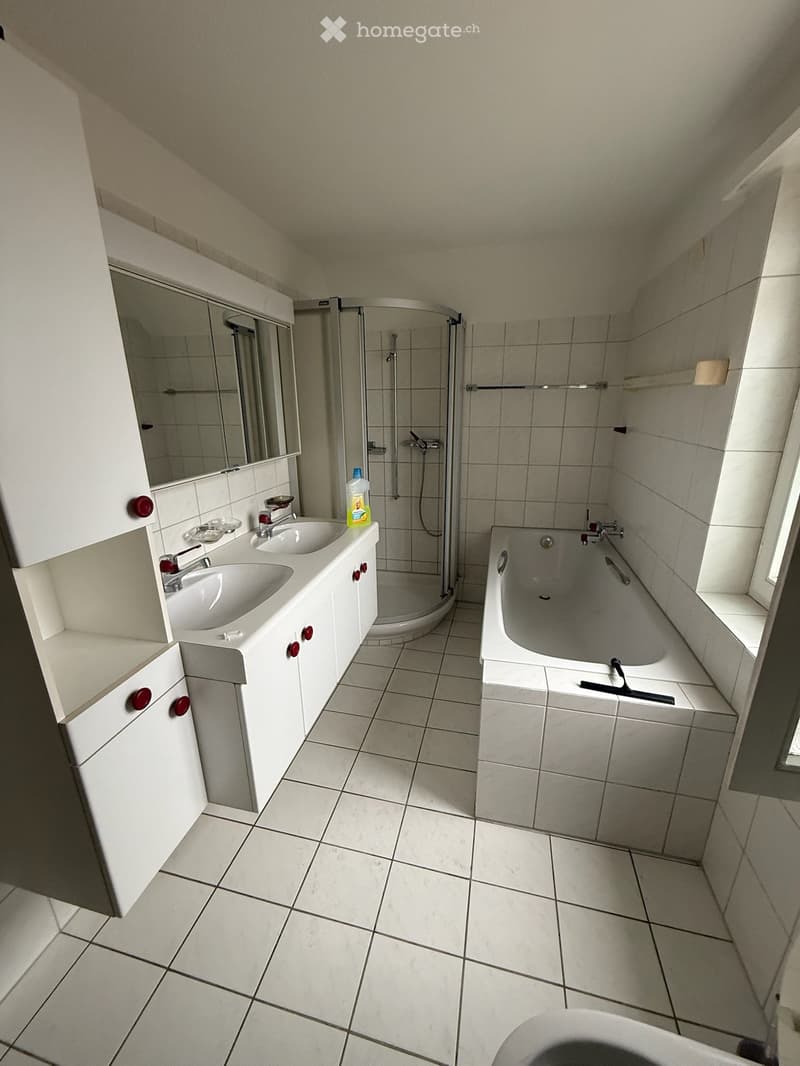 Modern bathroom with white tiled walls and floor, double sink vanity with mirror, bathtub, and walk-in shower with glass enclosure.
